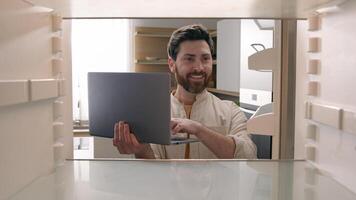 Hungry man guy open empty refrigerator confused find problem solution idea order food delivery laptop online buying products ordering goods with computer store app point of view POV from inside fridge photo