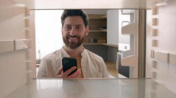 Hungry man guy open empty refrigerator poor crisis order food delivery with smartphone online buying products ordering goods with mobile phone store cellphone app point of view POV from inside fridge photo