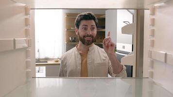 Man open empty refrigerator need food delivery shopping buying product smiling rise finger has good idea gesture find solution order meal courier smile happy insight point of view from inside fridge photo
