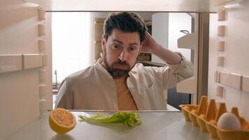 Hungry man guy open empty refrigerator with half lemon lettuce leaf one egg slice of bread leftover orange juice in bottle confused puzzled sad need food delivery point of view POV from inside fridge photo
