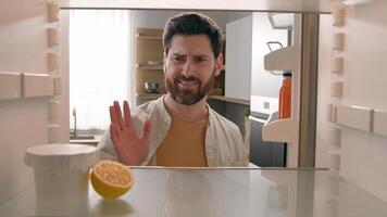 POV point of view from inside refrigerator hungry Caucasian man at kitchen open empty fridge with half of lemon and jam yogurt jar nothing to eat dissatisfied disgust close door food delivery service photo
