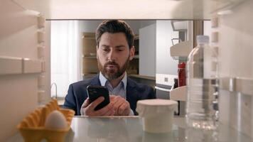 Point of view POV inside refrigerator Caucasian businessman employer man open fridge empty shelves with one egg and bottle of water order food with mobile delivery service buying products with phone photo