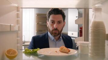 Hungry adult Caucasian businessman entrepreneur man after work open empty refrigerator with half lemon, lettuce leaf, bottle of milk and slice of bread eat crumbs POV point of view from inside fridge photo