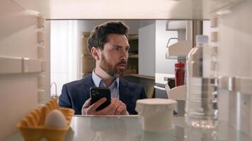 Point of view POV inside refrigerator Caucasian businessman employer man open fridge empty shelves with one egg and bottle of water order food with mobile delivery service buying products with phone photo