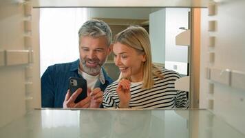 Point of view POV inside refrigerator Caucasian adult family mature couple middle-aged man woman open empty fridge order food with mobile delivery online service buying products with phone web store photo