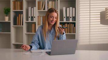 Multitasking Caucasian woman working with laptop writing in notebook talking mobile phone call loudspeaker happy businesswoman girl write notes typing computer record audio voice mail message studying photo