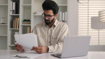 Focused man Arabian Indian ethnic businessman male employee manager writing notes business tasks data paperwork signing documents write on papers counting budget working with laptop computer in office photo