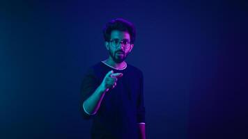 Neon ultraviolet background happy Indian guy Arabian man worker coder hacker computer engineer showing hey gesture pointing at camera smiling satisfied show thumbs up support good idea agree recommend photo