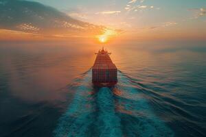A large cargo ship is sailing through the ocean with the sun setting in the background. The ship is the main focus of the image, and the sun's reflection on the water creates a serene photo