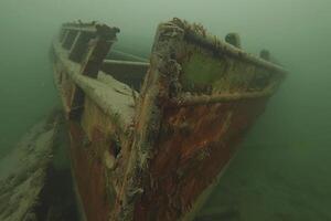 A shipwreck is seen in the ocean with a lot of debris and fish swimming around it. Scene is eerie and mysterious, as the ship is long gone and the ocean is filled with life photo