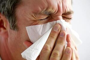 A handsome man is blowing his nose with a tissue during spring allergy season flowers blossom exhausted and uncomfortable allergens in air disease and sickness photo