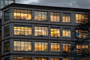 Modern office building windows lit in evening night early morning long working hours exhaustion overtime exterior urban architecture skyscraper lights tower financial sector banking hq photo