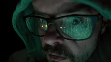 Hacker in hoody with beard and glasses, hacking and coding at night, reflection in glasses, facial expressions, closeup portrait video