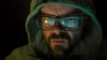 Hacker in hoody with beard and glasses, hacking and coding at night, reflection in glasses, facial expressions, closeup portrait video