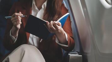 Asian business woman passenger sitting on business class luxury plane while working using smart phone mobile talking and use notebook while travel concept. video