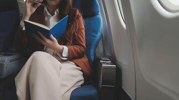 Asian business woman passenger sitting on business class luxury plane while working using smart phone mobile talking and use notebook while travel concept. video