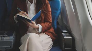 Asian business woman passenger sitting on business class luxury plane while working using smart phone mobile talking and use notebook while travel concept. video