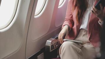 Asian business woman passenger sitting on business class luxury plane while working using smart phone mobile talking and use notebook while travel concept. video