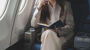 Asian business woman passenger sitting on business class luxury plane while working using smart phone mobile talking and use notebook while travel concept. video