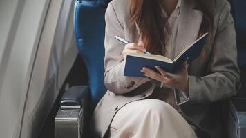Asian business woman passenger sitting on business class luxury plane while working using smart phone mobile talking and use notebook while travel concept. video