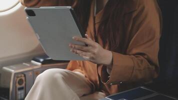 An Asian businesswoman in a semi-formal suit is using a tablet to read and analyze business data while traveling to a meeting in business class on a plane. video