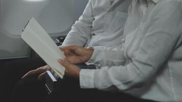 An Asian businesswoman in a semi-formal suit is using a tablet to read and analyze business data while traveling to a meeting in business class on a plane. video