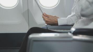 An Asian businesswoman in a semi-formal suit is using a tablet to read and analyze business data while traveling to a meeting in business class on a plane. video