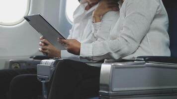 An Asian businesswoman in a semi-formal suit is using a tablet to read and analyze business data while traveling to a meeting in business class on a plane. video