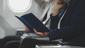 An Asian businesswoman in a semi-formal suit is using a tablet to read and analyze business data while traveling to a meeting in business class on a plane. video