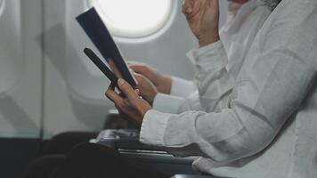 An Asian businesswoman in a semi-formal suit is using a tablet to read and analyze business data while traveling to a meeting in business class on a plane. video