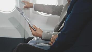 An Asian businesswoman in a semi-formal suit is using a tablet to read and analyze business data while traveling to a meeting in business class on a plane. video
