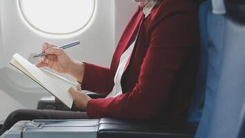 An Asian businesswoman in a semi-formal suit is using a tablet to read and analyze business data while traveling to a meeting in business class on a plane. video