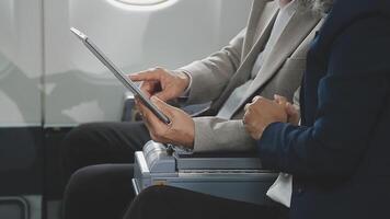 An Asian businesswoman in a semi-formal suit is using a tablet to read and analyze business data while traveling to a meeting in business class on a plane. video