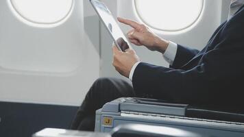 An Asian businesswoman in a semi-formal suit is using a tablet to read and analyze business data while traveling to a meeting in business class on a plane. video