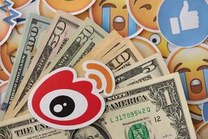 KYIV, UKRAINE - APRIL 20, 2024 Weibo logo and many usd money bills. Symbol of famous social network platform and dollar currency banknotes on lot of emoji reactions photo