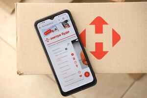 KYIV, UKRAINE - APRIL 20, 2024 Nova Poshta Logotype on cardboard box and website on smartphone screen. Nova Poshta is best ukrainian postal service company photo