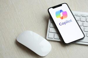 KYIV, UKRAINE - MARCH 17, 2024 Microsoft Copilot logo on iPhone display screen with apple keyboard and mouse on table photo