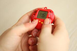 KYIV, UKRAINE - MARCH 9, 2024 Retro pet keychain game tamagotchi in red plastic case in female hands photo
