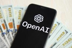KYIV, UKRAINE - MARCH 17, 2024 OpenAI logo on iPhone display screen with many hundred dollar bills photo
