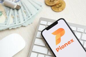 KYIV, UKRAINE - MARCH 15, 2024 Pionex logo on iPhone display screen on white keyboard with money and bitcoins photo