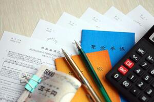 Japanese pension insurance booklets on table with yen money bills, pen and calculator on table photo