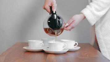 Hand pouring tea into multiple cups on a wooden table. video