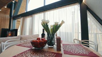 A beautifully set dining table with a vase of white tulips and a bowl of tangerines, placed near large windows. video