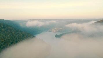 A top view of the morning fog that spread over the river. A beautiful view of the river canyon through the misty clouds. A recreation center in a picturesque canyon. Aerial view video