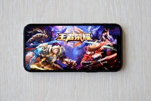 Honor of Kings mobile iOS game on iPhone 15 smartphone screen on wooden table during mobile gameplay photo