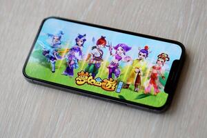 Fantasy Westward Journey mobile iOS game on iPhone 15 smartphone screen on wooden table during mobile gameplay photo