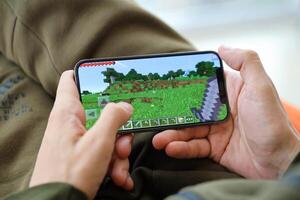 Minecraft mobile iOS game on iPhone 15 smartphone screen in male hands during mobile gameplay photo