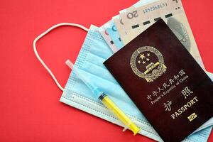 Red passport of People Republic of China and chinese yuan money bills with syringe and mask photo