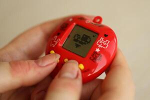 KYIV, UKRAINE - MARCH 9, 2024 Retro pet keychain game tamagotchi in red plastic case in female hands photo
