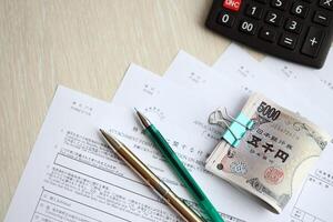Japanese tax forms lies on table with calculator, pen and japanese yen money bills roll photo